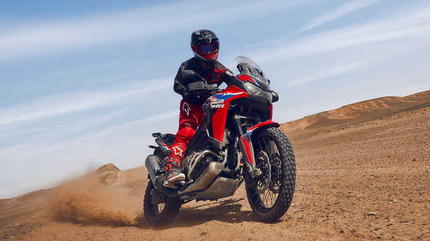 Fotómodell ül egy CRF1100L Africa Twin motorkerékpáron a sivatagban.