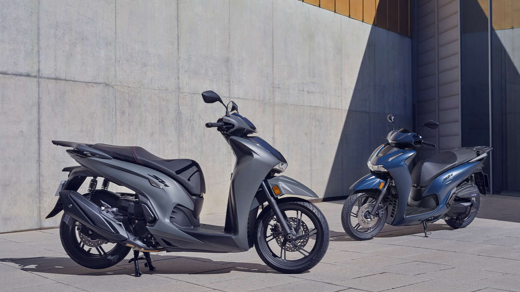 Két SH350i motorkerékpár egy betonfal előtt.